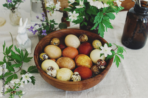 Canvas Print Stylish easter eggs in wooden bowl on rustic table with bunny and blooming flowers