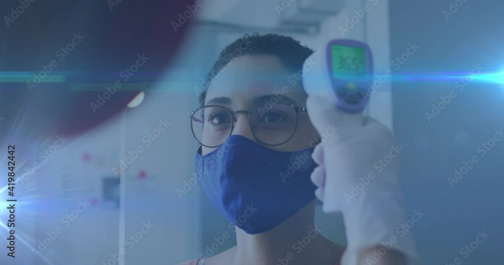 Animation of glowing light trails over woman wearing face mask having temperature checked Animation of glowing light trails over woman wearing face mask having temperature checked