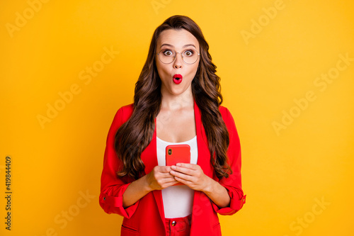 Photo of lovely young woman hold telephone shocked expression wear red blazer spectacles isolated vibrant yellow color background
