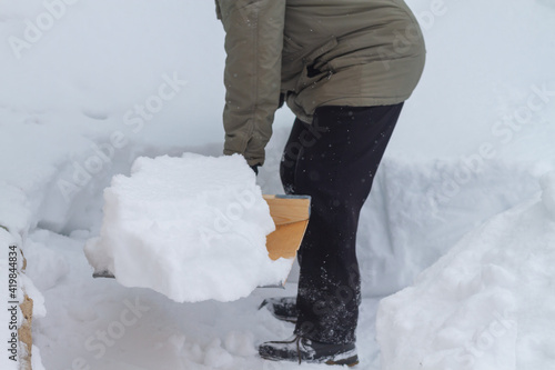 A man clears the snow with a wooden shovel in winter