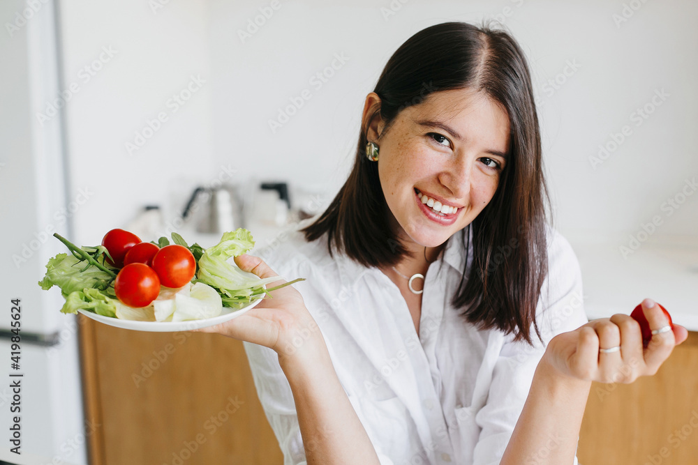 Happy woman holding plate with fresh lettuce, cherry tomatoes, arugula in kitchen. Healthy eating Happy woman holding plate with fresh lettuce, cherry tomatoes, arugula in kitchen. Healthy eating