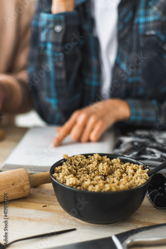 Cooked quinoa porridge is on the table along with salad. Cooking process in the kitchen. Kitchen utensils and ambiance. In the background, a family is reading a recipe.