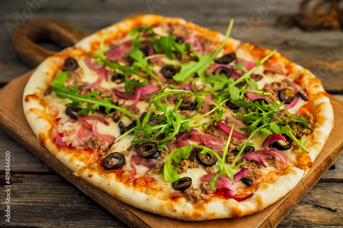 Pizza with minced meat  black olives  onion  rocket salad  cheese and tomato sauce  on wooden board  wooden rustic backdrop