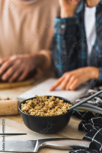 Cooked quinoa porridge is on the table along with salad. Cooking process in the kitchen. Kitchen utensils and ambiance. In the background, a family is reading a recipe.