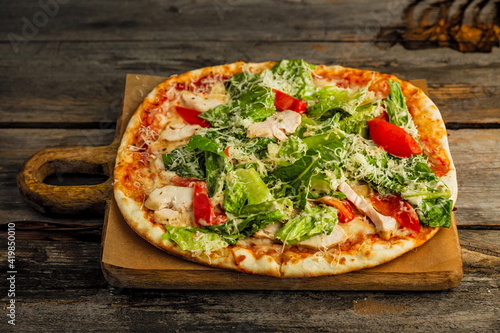 Pizza with caesar salad. Chicken meat, tomatos, lettuce, sauce, grated cheese, on wooden board, rustic wooden backdrop
