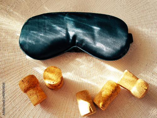 A soft cloth sleep mask and wine bottle corks are set against a light woven background. The concept of rest after an alcoholic party, recuperation, health recovery. Eye protection from bright light.