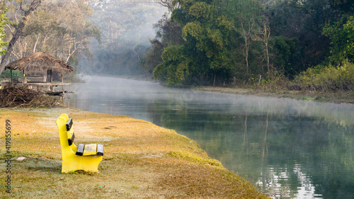 A yellow bench and sheds on the bank of a canal in Thakurdwara, Thakurbaba of Bardiya in Nepal. Thakurdwara is an relaxing travel destination for nature lovers in Bardiya National Park.