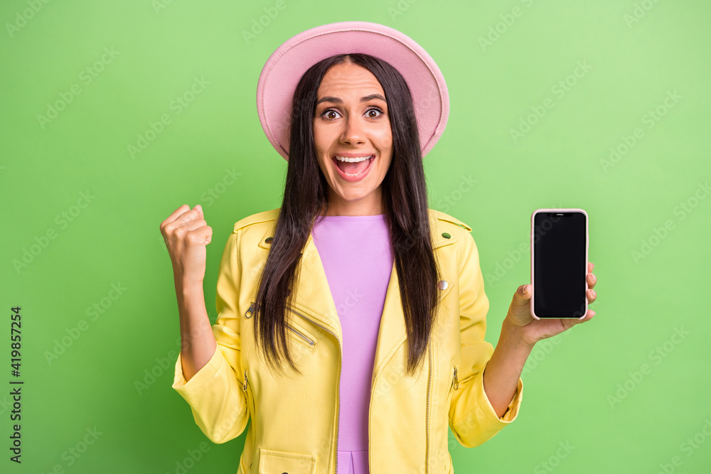 Photo of funny girl hold cellphone screen empty space open mouth wear yellow jacket pink hat isolated green color background Photo of funny girl hold cellphone screen empty space open mouth wear yellow jacket pink hat isolated green color background