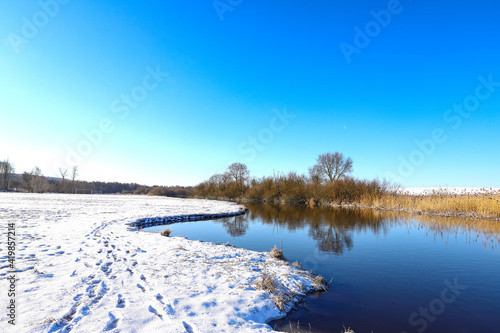 Winter river, panoramic view of the picturesque winter-spring landscape at sunrise. Bright blue sky, frozen shore, snow, ice. © Stepanych