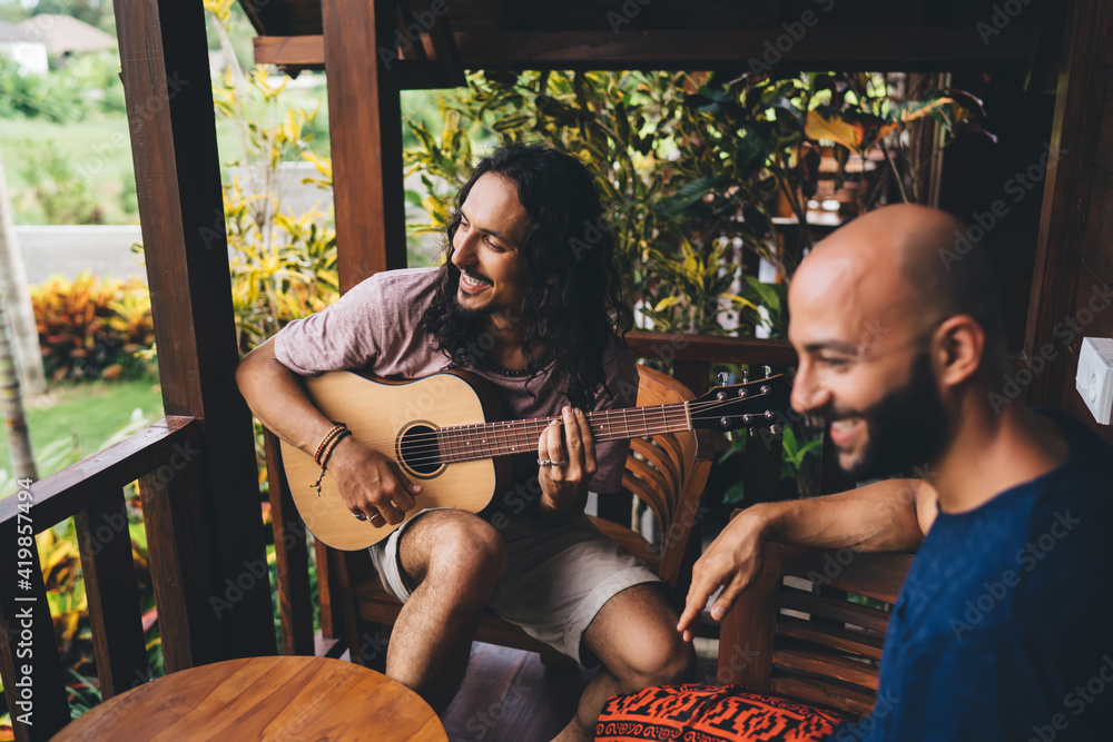 Optimistic multiracial friends playing guitar on terrace
