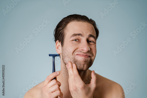 Close up portrait of a young shirtless man shaving