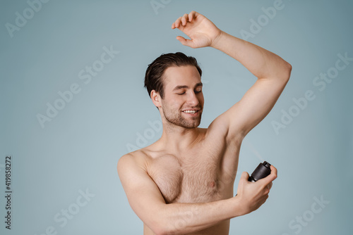 Handsome smiling nude man spraying deodorant