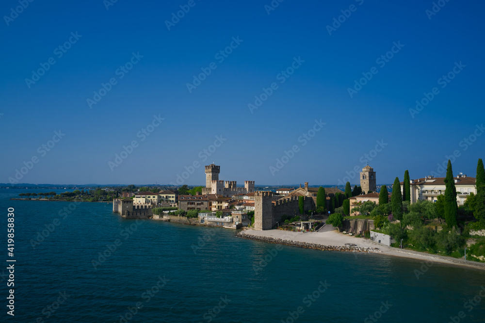 View by Drone. Rocca Scaligera Castle in Sirmione. Aerial view on Sirmione sul Garda. Italy, Lombardy. Amazing view to the old bridge and harbor of Sirmione.