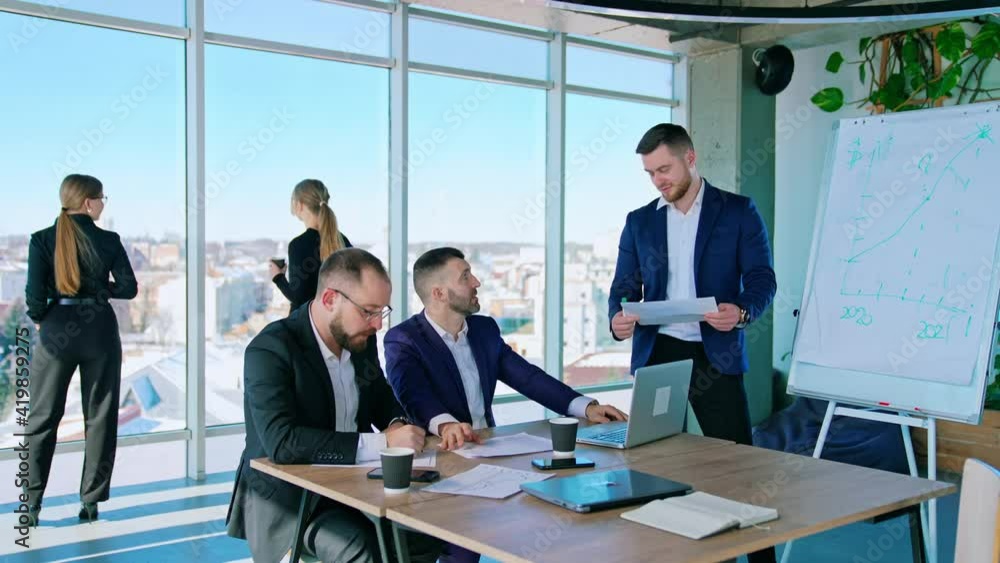 Teamwork of business colleagues. Businessman partners at table negotiate about a new blueprint. Young pretty female managers standing near the large window. Teamwork of business colleagues. Businessman partners at table negotiate about a new blueprint. Young pretty female managers standing near the large window.