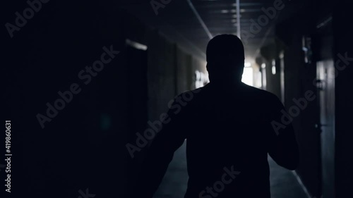 The silhouette of a man runs down a dark corridor to the light at the end and waves his arms and hurries. A man in baggy Indian pants. Rear view.