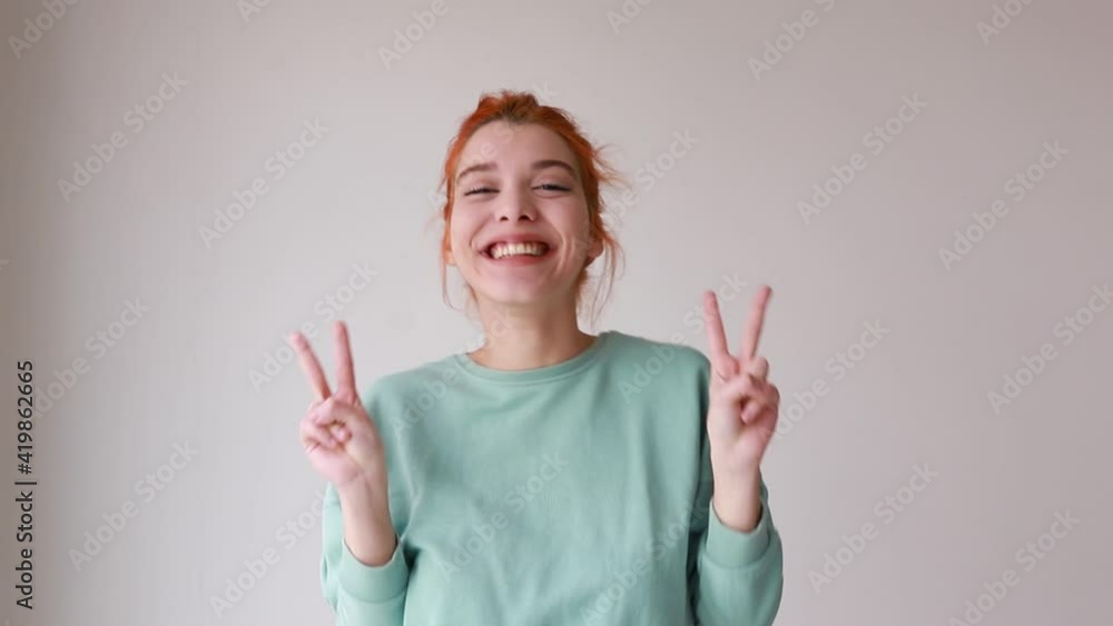 Young red hair woman smiling and showing victory sign with a cheerful face over isolated background Young red hair woman smiling and showing victory sign with a cheerful face over isolated background