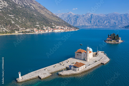 Aerial shot, drone flies above the blue sea to two small Islands. On one island there is a Christian church, on the second there are residential buildings and coniferous trees. Mountains and coastline photo