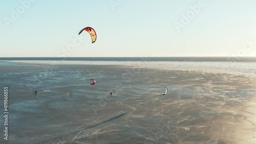 Beautiful drone shot of kite boarding over frozen sea in a sunny day. Camera pan to left. 4k footage