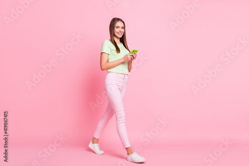 Full body profile portrait of charming positive person walking look camera isolated on pink color background