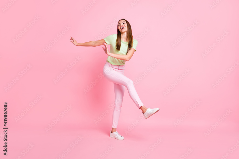 Full length photo of adorable funny young lady wear green t-shirt dancing isolated pastel pink color background
