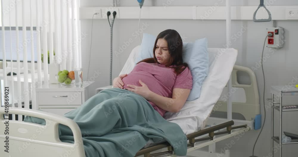 Pregnant woman lying in patient bed having stomach aches Pregnant woman lying in patient bed having stomach aches