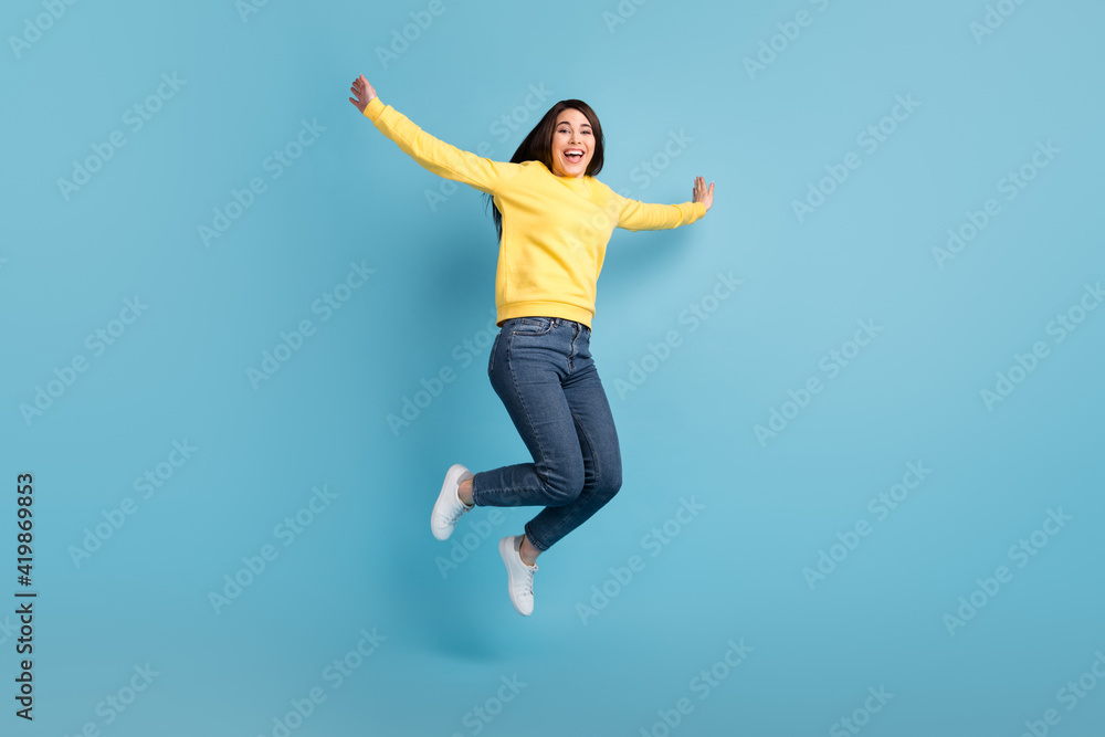Photo of excited crazy lady jump raise hands open mouth wear yellow jumper jeans sneakers isolated blue background