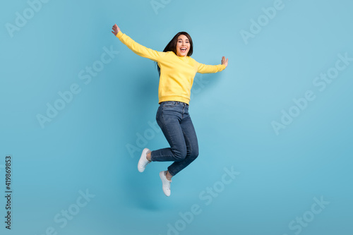 Photo of excited crazy lady jump raise hands open mouth wear yellow jumper jeans sneakers isolated blue background © deagreez