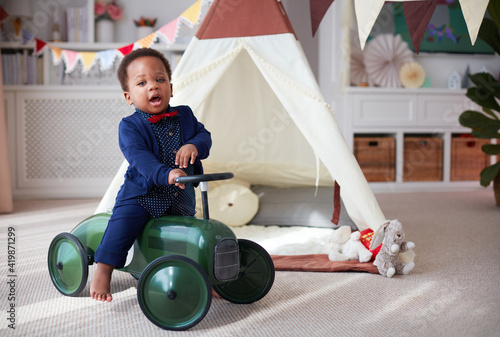 cute one year old baby boy having fun on a push car in a nursery room at home photo