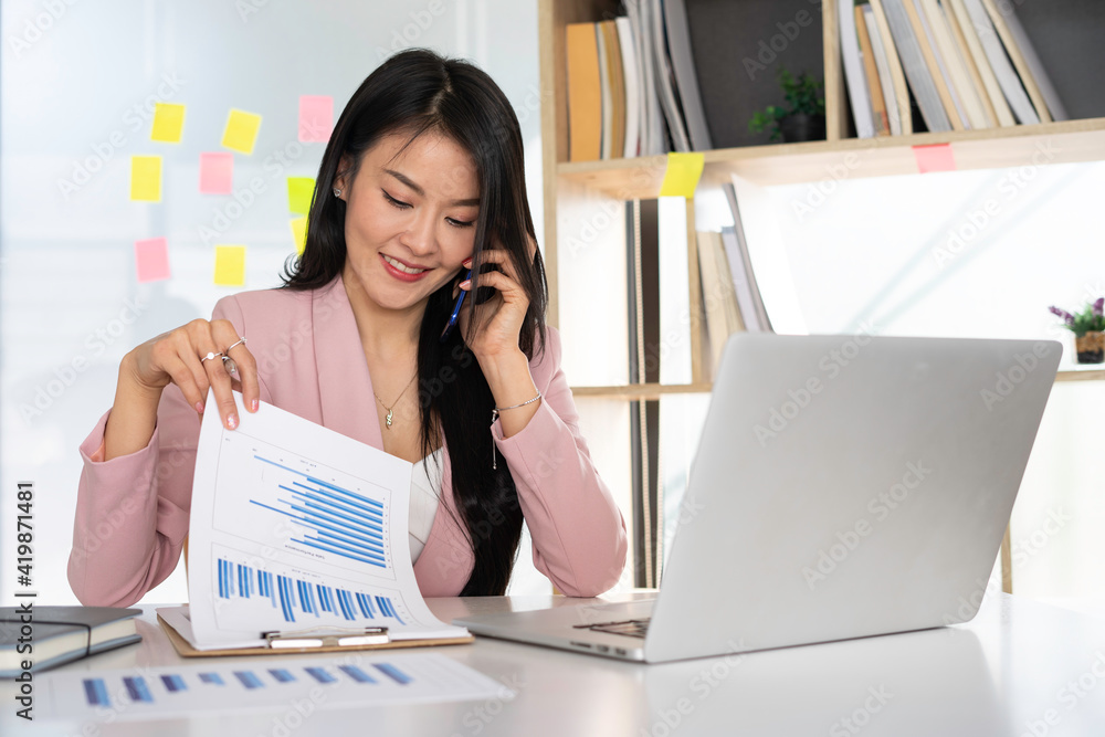 Positive Asian Women Finance is on a conference call with partners to summarize the company's sales. A beautiful money manager in a pink suit is making a phone call in the office Positive Asian Women Finance is on a conference call with partners to summarize the company's sales. A beautiful money manager in a pink suit is making a phone call in the office