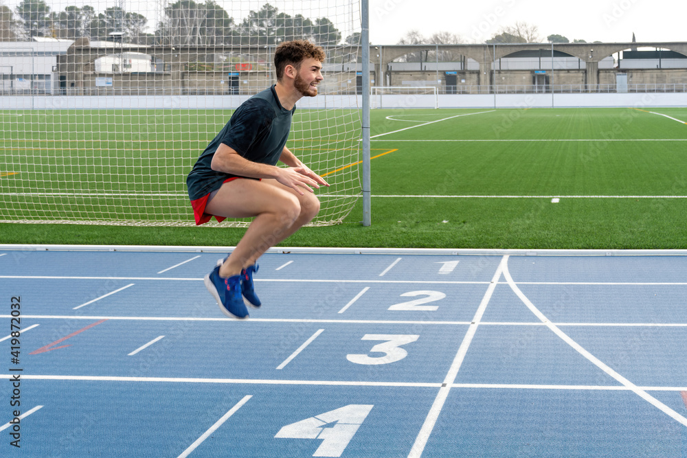 Obraz premium Hard working young runner boy doing warm-up in blue running track.