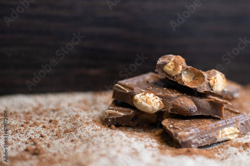Chocolate with nuts, migdal. On a light dark background
place for text. 
Broken pieces of chocolate and cocoa powder on wooden background