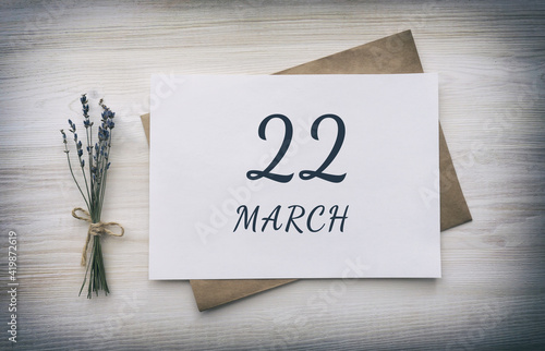 march 22. 22th day of the month, calendar date. White blank of paper with a brown envelope, dry bouquet of lavender flowers on a wooden background. Spring month, day of the year concept