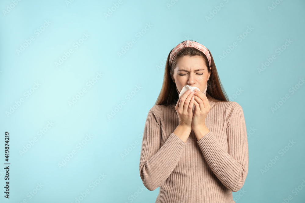 Young woman with tissue suffering from runny nose on light blue background. Space for text Young woman with tissue suffering from runny nose on light blue background. Space for text