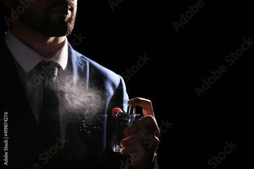 Man spraying luxury perfume on black background, closeup photo
