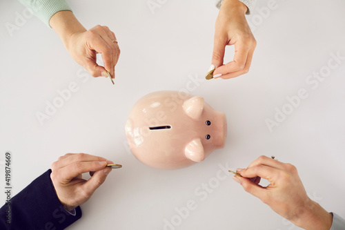 Fotografía Hands putting money in pink piggy bank on white table background