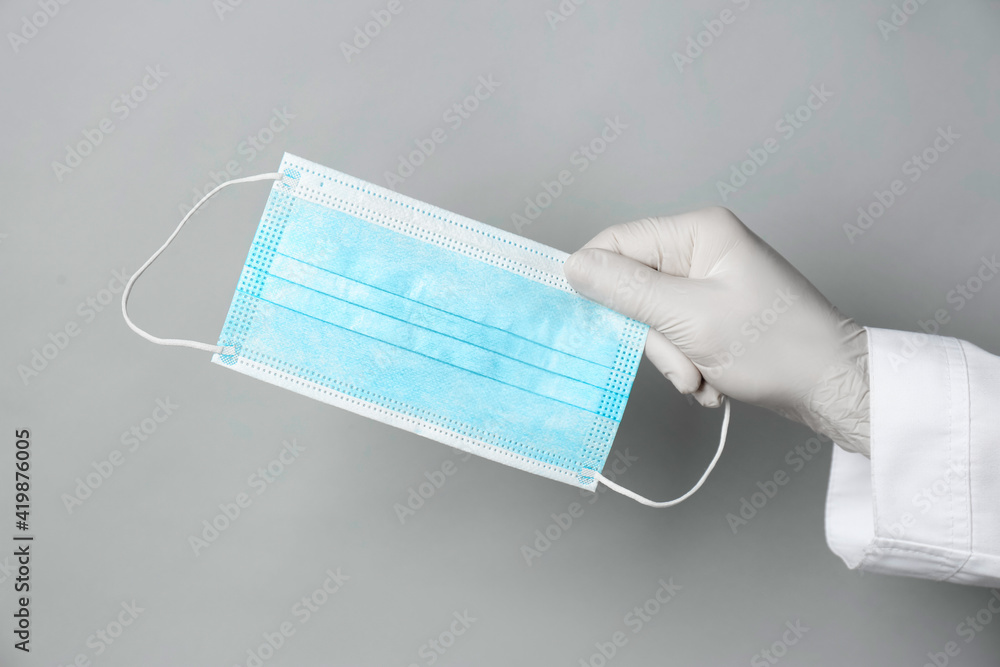 Doctor in medical gloves holding protective mask on light grey background, closeup Doctor in medical gloves holding protective mask on light grey background, closeup