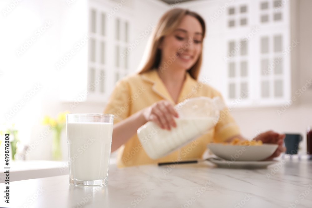 Woman with gallon bottle and breakfast cereal at white marble table in kitchen, focus on glass of milk Woman with gallon bottle and breakfast cereal at white marble table in kitchen, focus on glass of milk