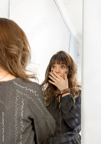 Emotional beautiful young brunette stands at the mirror and makes faces.