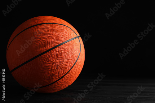 Basketball ball on black wooden table against dark background, space for text © New Africa