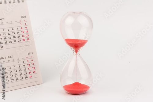Time passing concept. Crystal hourglass with red sand and calendar on light background