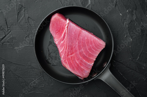 Raw tuna steak, fresh red tuna fish fillet , on frying cast iron pan, on black stone background, top view flat lay , with copyspace and space for text