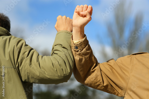 People greeting each other by bumping elbows instead of handshake outdoors, closeup