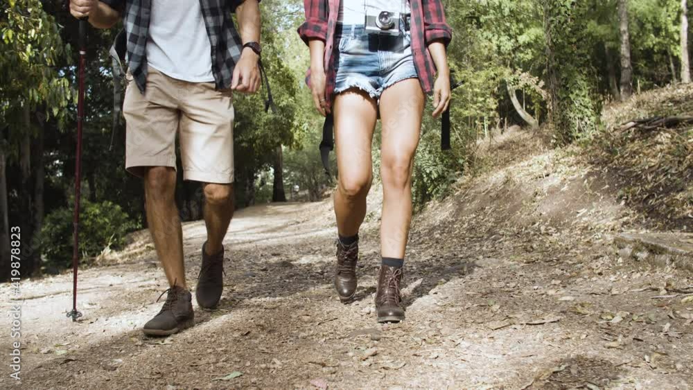 Legs of hikers wearing shorts and trekking boot, walking on forest path