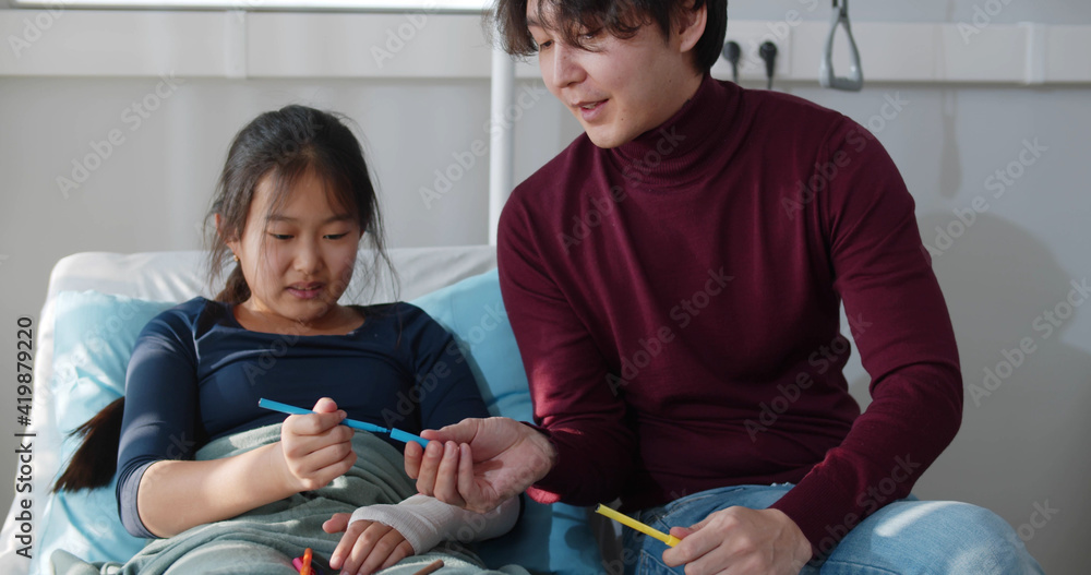 Asian man visiting sick teen sister in hospital and painting together