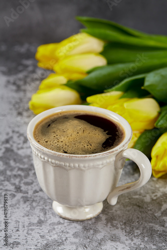 cup of black coffee on stone surface and bouquet of yellow tulips