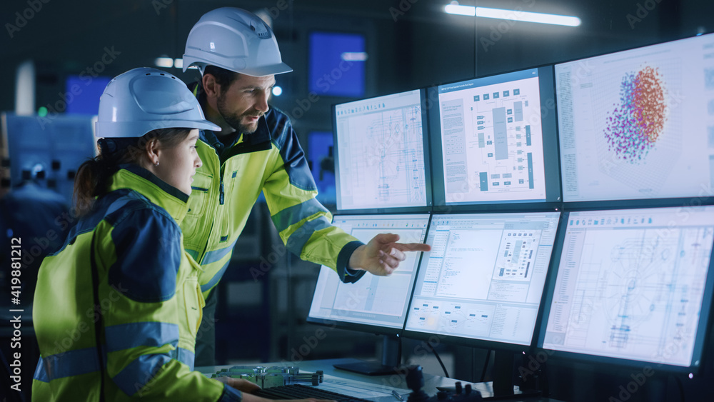 Industry 4.0 Modern Factory: Chief Project Manager Talks to Female Engineer, She Points at Computer Screens Showing Complex Industrial Electronics Design Blueprints, They Have Find Problem Solution Industry 4.0 Modern Factory: Chief Project Manager Talks to Female Engineer, She Points at Computer Screens Showing Complex Industrial Electronics Design Blueprints, They Have Find Problem Solution