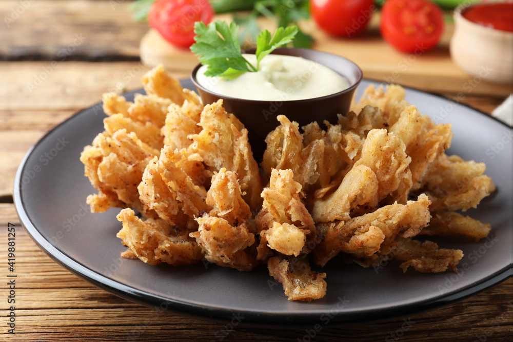 Fried blooming onion with dipping sauce served on wooden table, closeup Fried blooming onion with dipping sauce served on wooden table, closeup