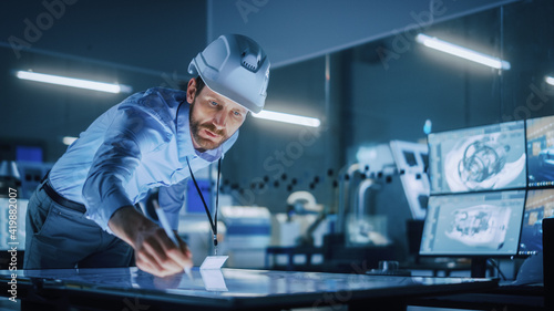 Industry 4.0 Modern Factory Office Meeting Room: Handsome Male Engineer Wearing Hardhat, Uses Pen on Touchscreen Digital Table to Correct, Draw Machinery Blueprints. High-Tech Electronics Facility 