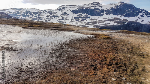 A paddle, deriving from the melting snow spreading on a barren meadow. Taller mountains in the back covered with snow. Nature wakes up after long winter vegetation.