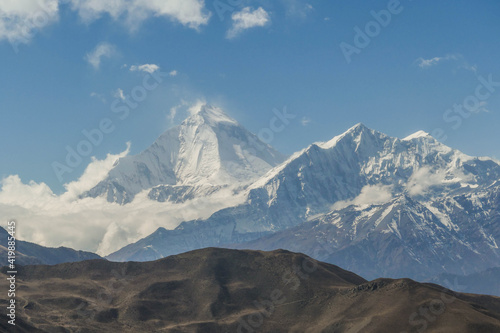 A brown hill and in the background sharp, snowy and high mountain peaks in the Himalayas in Nepal. .